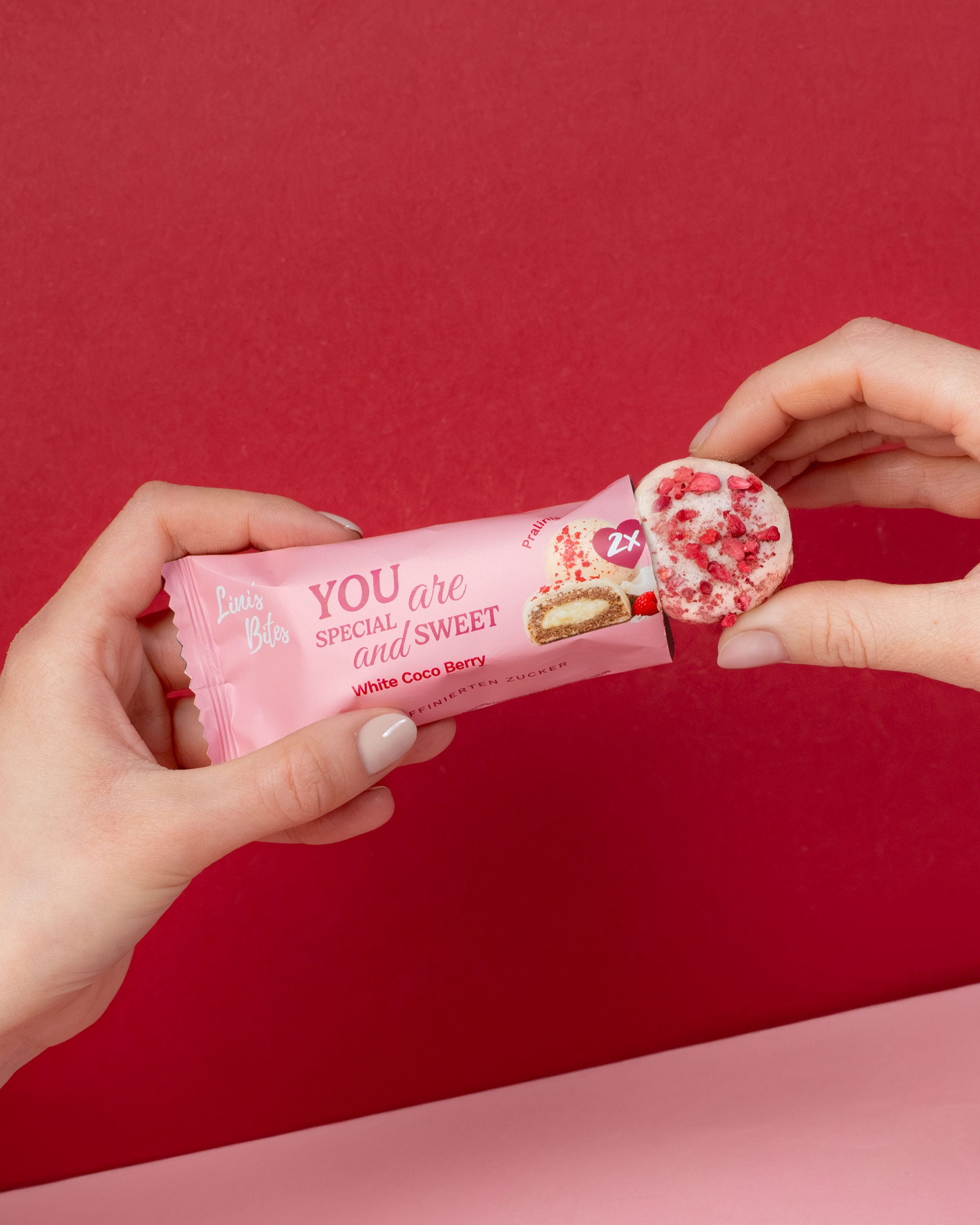 Weiße Pralinis von Linis Bites – Energy Ball-Praline Hybrid, Sorte White Coco Berry – Detailansicht und Verpackungsansicht mit Händen